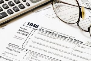 Eyeglasses and a calculator placed on top of a printed IRS 1040 form and other related documents